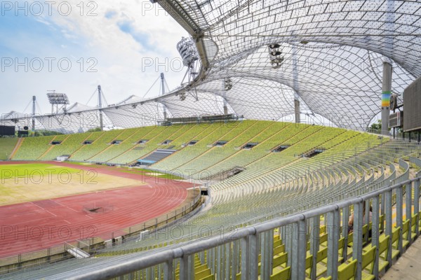 Large stadium with empty green stands and striking roof structure in the sunlight, Olympiapark, Munich, Germany