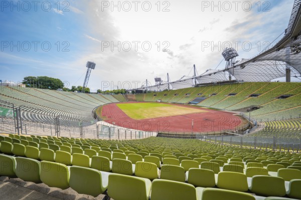 Empty stadium with green seats and a red running track under a bright sky, Olympiapark, Munich, Germany