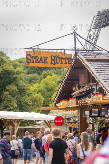 Traditionally designed hut with lettering, surrounded by people and green background, Olympic Park, Munich, Germany