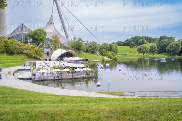 Idyllic landscape with lake, modern pavilion and grassy hills, Olympic Park, Munich, Germany