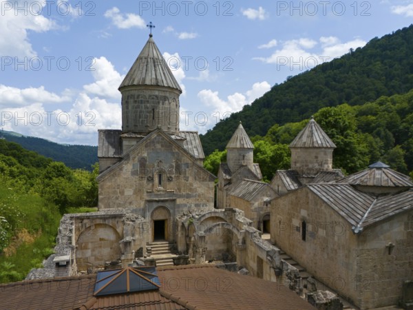 Historic stone monastery surrounded by green forests under a blue sky with clouds, aerial view, Haghartsin Monastery, Hagarzin, left Surp Astvatsatsin Church, right Surp Stepanos and Surp Grigor Church and a Gavit, Tavush Province, Armenia