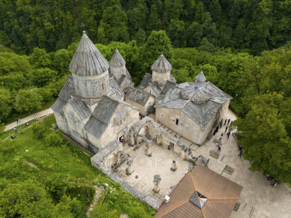 Stone monastery with visitors, surrounded by forest and hilly terrain, aerial view, Haghartsin Monastery, Hagarzin, on the left Surp Astvatsatsin Church, on the right Surp Stepanos and Surp Grigor Church and a Gavit, Tavush Province, Armenia