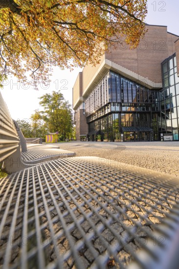 Modern building with glass front, framed by autumnal trees, urban and sunny ambience, Munich, Germany