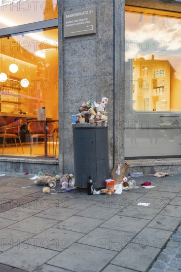 An overfilled rubbish bin with waste on the pavement in front of a shop, Marienplatz, Munich, Germany