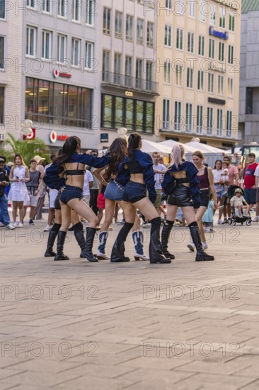 Dance group performs outdoors against an urban backdrop, surrounded by spectators, Munich, Germany