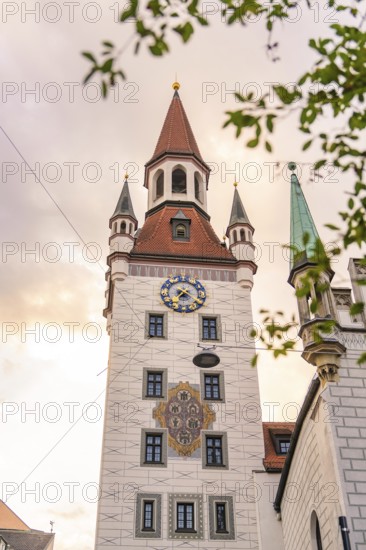 Baroque tower with red roofs and clock in front of a gold-coloured sky, Munich, Germany
