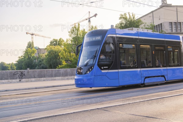 Blue tram travelling on a road along the tracks, urban scenery with construction cranes, Munich, Germany