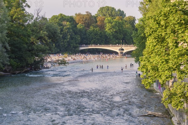 River with people crossing the bridge and relaxing on the bank, surrounded by green nature, Munich, Germany