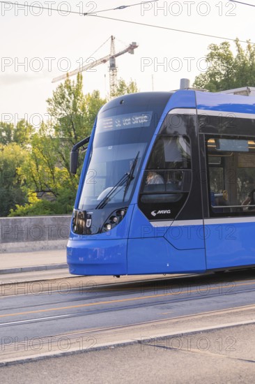 Modern blue tram travelling on a city street, construction cranes visible in the background, Munich, Germany