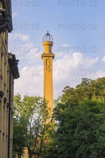 High yellow tower rises into the blue sky, framed by green trees on a sunny day, Munich, Germany