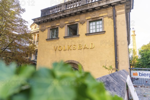 Historic public swimming pool with yellow façade, traditional architecture and surrounded by trees, Munich, Germany