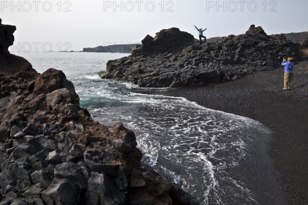 On the black lava beach Djúpalónssandur with young female tourists photographing and posing, Snæfellsnes, West Iceland, Iceland