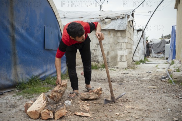 A young displaced Syrian man cutting firewood to use for heating inside a refugee camp. Aleppo, Syria February 9, 2018, Aleppo, Syria
