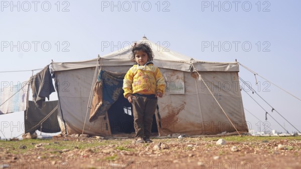 A Syrian girl stands in front of her tent in a refugee camp. World Children's Day. Aleppo, Syria. January 25, 2023, Aleppo, Syria