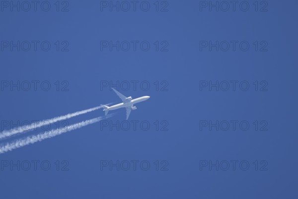 Jet passenger aircraft with a vapour trail or contrail flying in a blue sky, England, United Kingdom