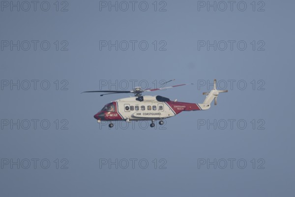 Sikorsky S-92A helicopter of the UK HM Coastguard flying in a blue sky, England, United Kingdom