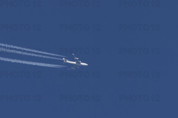 Boeing 747 jumbo jet cargo aircraft with a vapour trail or contrail flying in a blue sky, England, United Kingdom