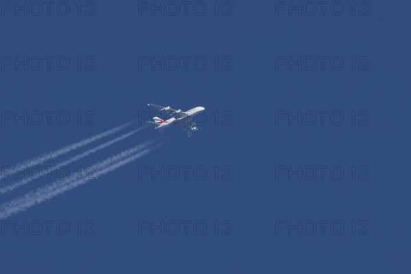 Airbus A380 jet passenger aircraft of Emirates airlines with a vapour trail or contrail flying in a blue sky, England, United Kingdom