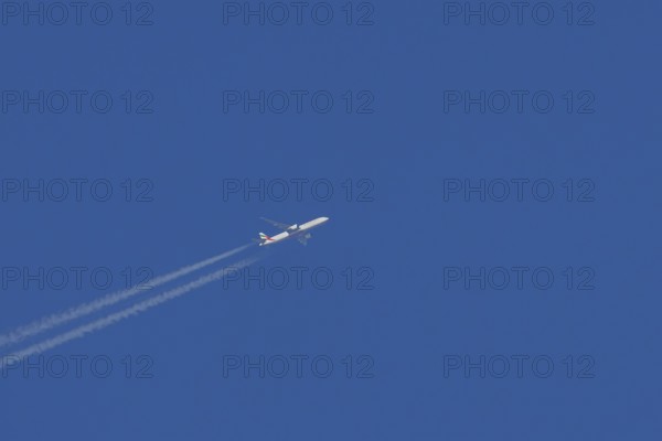 Airbus jet passenger aircraft of Emirates airlines flying with vapour trails or contrails behind in a blue sky, England, United Kingdom