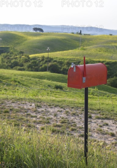 Red standing letterbox in a field with lush green hills in the background, Tuscany, Italy
