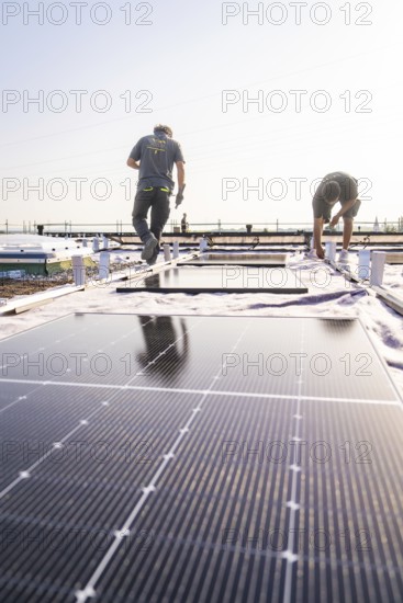 Two workers install solar panels on a sunny roof, PV installation, commercial customers, new build, Pforzheim, Germany