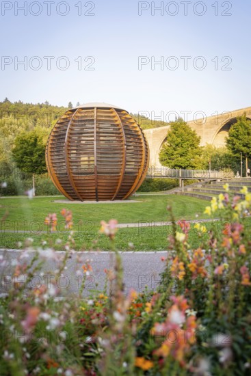 Wooden sculpture in a park with flowers and bridge in the background under a clear sky, Nagold, district of Calw, Black Forest, Germany