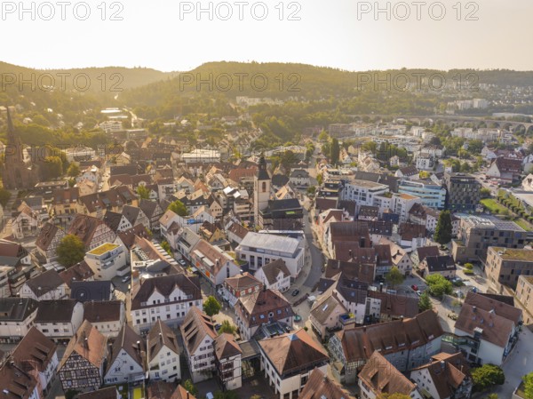Urban landscape with densely packed houses and a church, behind them rolling hills in the light, Nagold, district of Calw, Black Forest, Germany