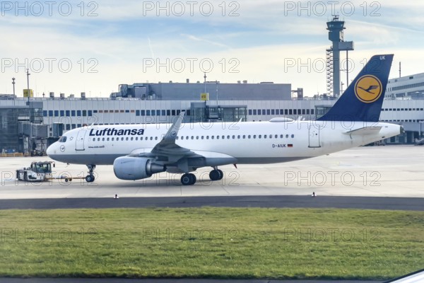 Lufthansa Airbus A320-200 being towed by a tug on the apron, in the background terminal and modern high tower airport tower, Düsseldorf International Airport DUS, Düsseldorf, North Rhine-Westphalia, Germany