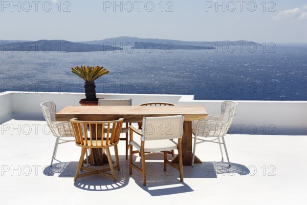 Wooden table and various chairs on a white terrace by the sea, view of the caldera, Oia, Santorini, Cyclades, Aegean Sea, Greece