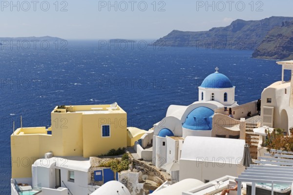 Yellow holiday home by the sea, with typical roof terrace, orthodox church with blue dome, view into the caldera, Oia, Thira, Santorini, Cyclades, Greece