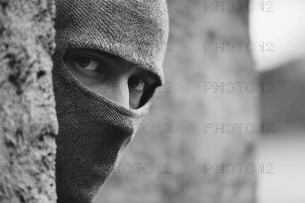 Mann in Kapuzenpullover schaut mit intensivem Blick hinter einer Mauer und beobachtet eine Situation, Symbolbild für Einbrecher, Gangster, Krimineller, Kriminalität, Verbrecher, Dieb, bedrohliche und beängstigende Stimmung, AI generiert, AI generated