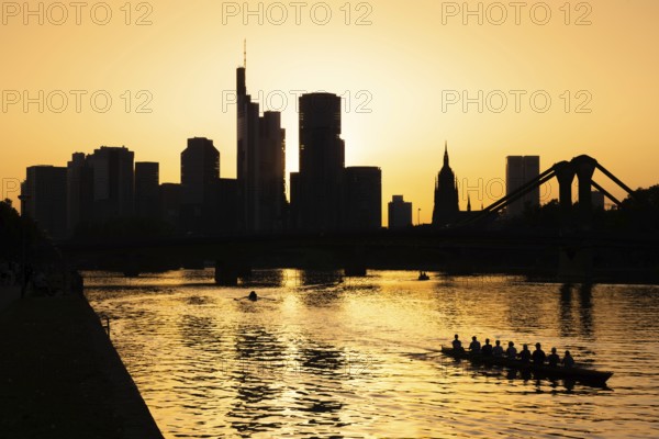 A rowing boat navigates the Main as the sun sets behind the Frankfurt banking skyline, Frankfurt am Main, Hesse, Germany