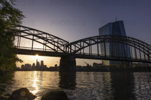 The sun stands over the Frankfurt banking skyline and illuminates the glass façade of the European Central Bank (ECB), Frankfurt am Main, Hesse, Germany