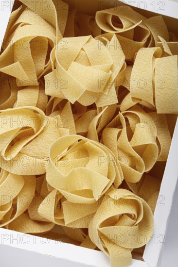 Raw pappardelle pasta, pasta nests, in a paper box, top view, no people
