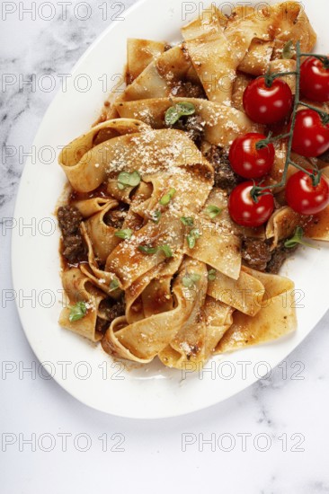 Pappardelle pasta with bolognese sauce, topped with parmesan cheese and cherry branch, homemade, no people
