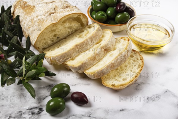 Appetizer, sliced ciabatta bread, with olive oil, green olives, Chalkidiki olives, classic Green green olive, on a marble table, top view, no people