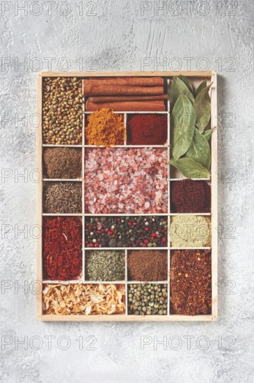 An assortment of spices laid out on a wooden tray, arranged in wooden compartments, top view