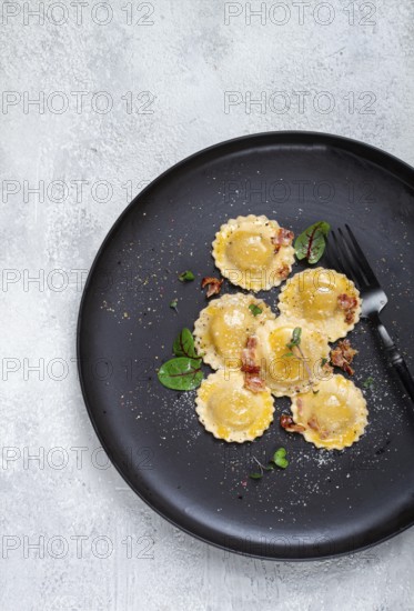Fresh ravioli, with butter, spices and herbs, fried bacon, on a black plate, top view, dark background, no people
