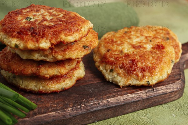 Crispy potato pancakes Latkes, stacked on a wooden board next to fresh green onions, natural light, homemade, no people