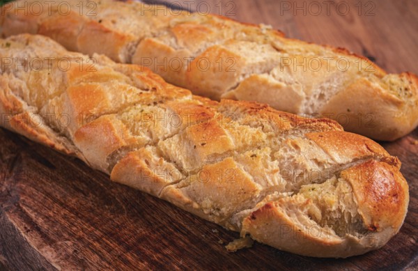 Garlic bread, baguette with garlic butter and herbs, on a wooden board, with herbs and garlic cloves
