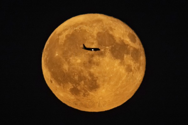 The silhouette of an aeroplane stands out against the full moon, Frankfurt am Main, Hesse, Germany