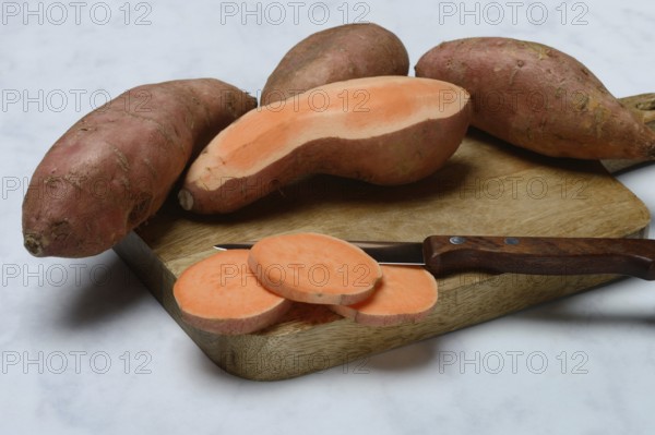 Sweet potatoes with kitchen knife on wooden board, Ipomoea batatas
