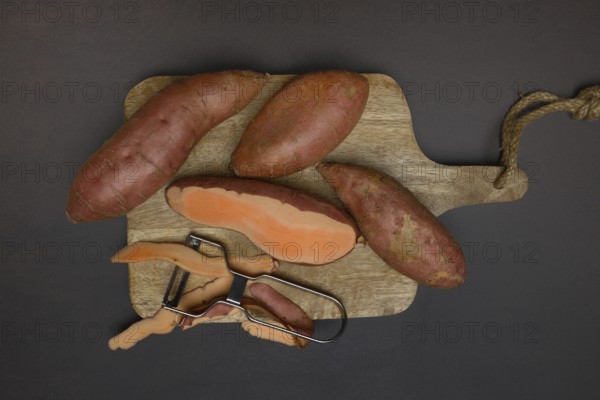Sweet potatoes with potato peeler on wooden board, Ipomoea batatas