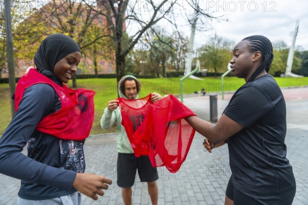 Diverse friends smiling and gearing up on an outdoor urban basketball court, putting on team bibs and bonding before a casual game, showcasing teamwork and healthy activity