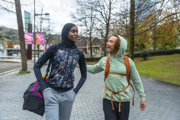 Diverse young adult friends wearing activewear walking and talking in an urban park, sharing a moment of connection and enjoyment during their active outdoor lifestyle