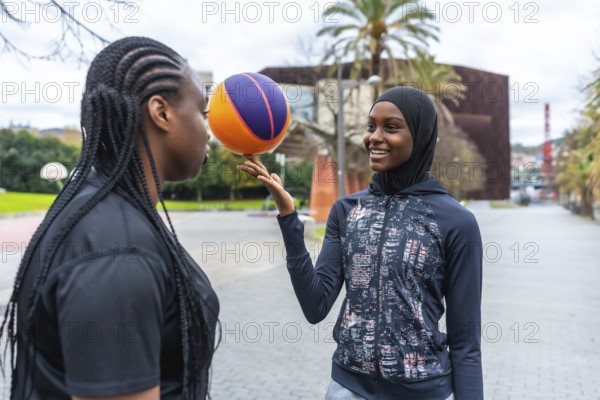 Two diverse young women enjoying a friendly basketball game at an outdoor court, one skillfully balancing the ball on her finger while smiling at her friend