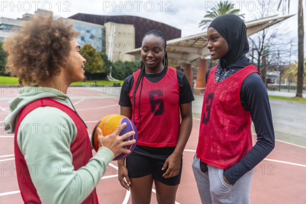 Young diverse athletes wearing sports bibs, holding a basketball, and talking on an urban court, reflecting teamwork, inclusion, and a healthy lifestyle