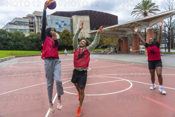 Diverse young friends actively competing in a street basketball game on an outdoor court, jumping for the ball and enjoying camaraderie and healthy lifestyle