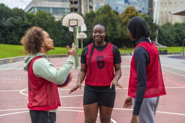 Diverse young adults on an urban basketball court talking strategy and bonding over streetball, collaborating as a confident, happy team during outdoor practice and play