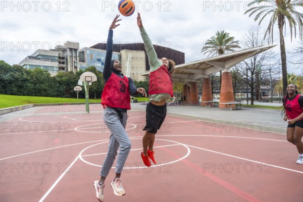Diverse young women are jumping and reaching for a ball during a friendly outdoor basketball game on a court, showcasing teamwork, competition, and an active lifestyle